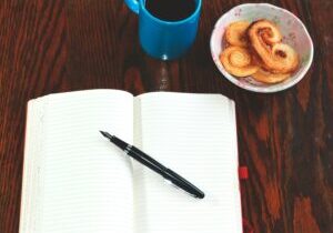 journal on a desk next to a blue mug of coffee and danish